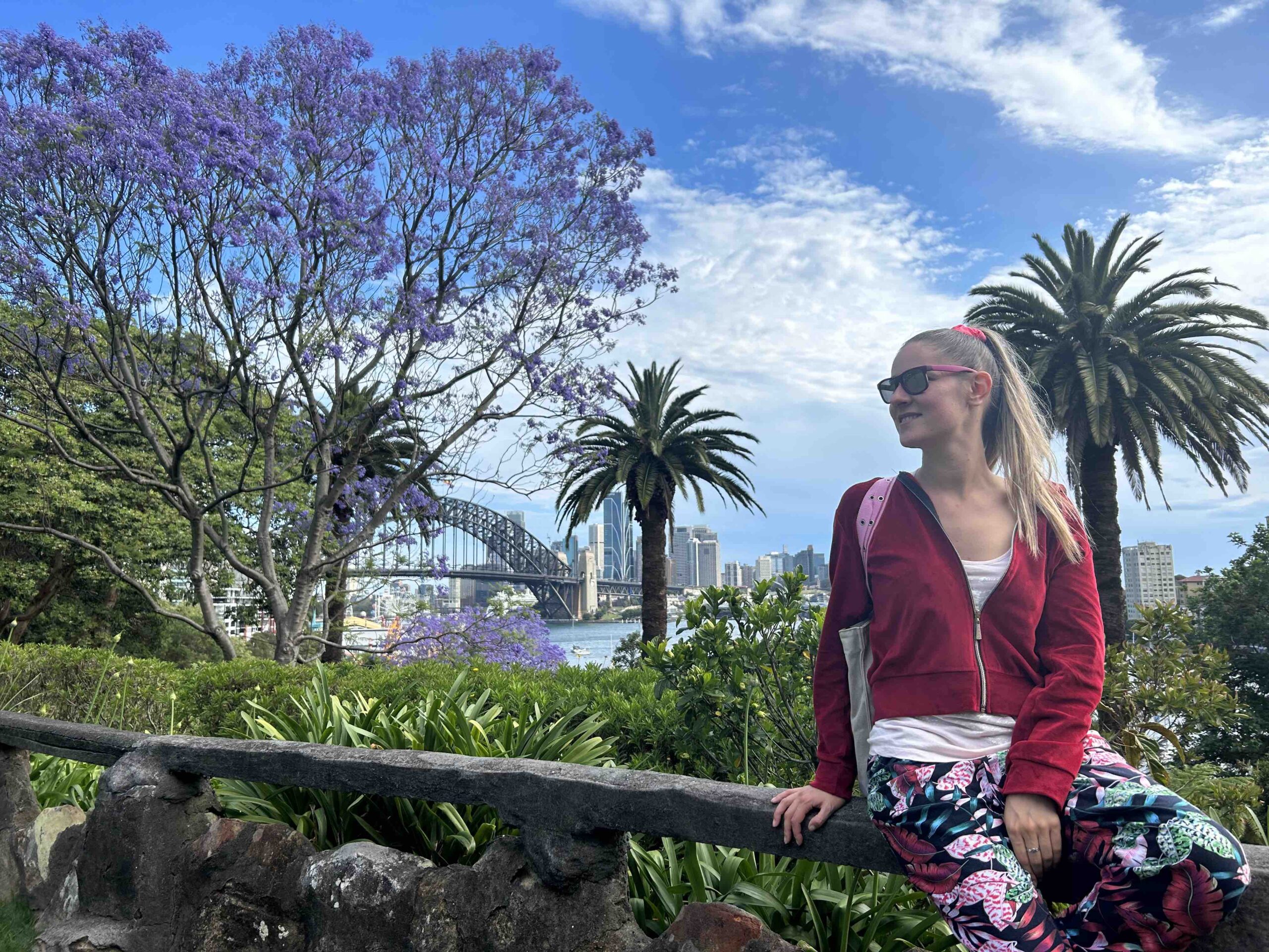 Viaggiatrice in un parco con palme, alberi in fiore e cielo azzurro